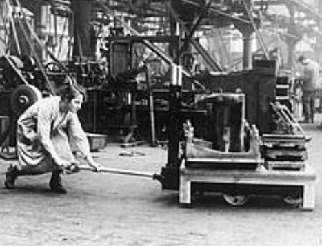 Factory worker pushing a hand pallet jack beside large industrial machinery in a factory