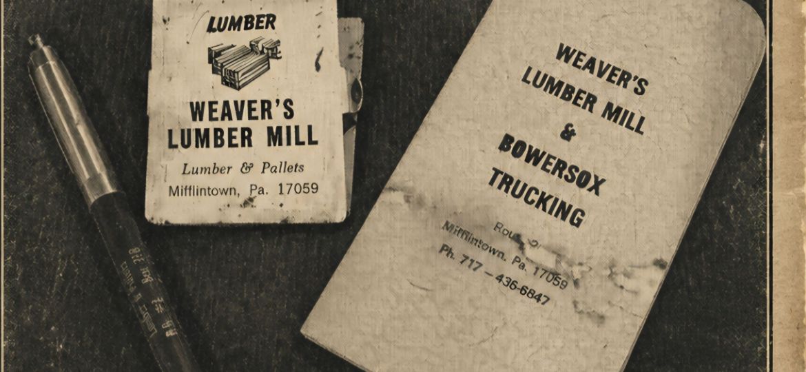 Vintage desk scene with Weaver's Lumber Mill promotional materials and a small labeled card on a dark surface, including a metal case and a folded paper.