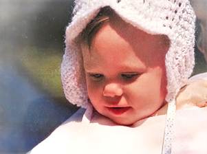 Close up of a baby wearing a white knit bonnet looking down in sunlight
