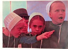 Four children in pale nurse outfits and caps lean forward as one points ahead suggesting guidance or emphasis on something off screen